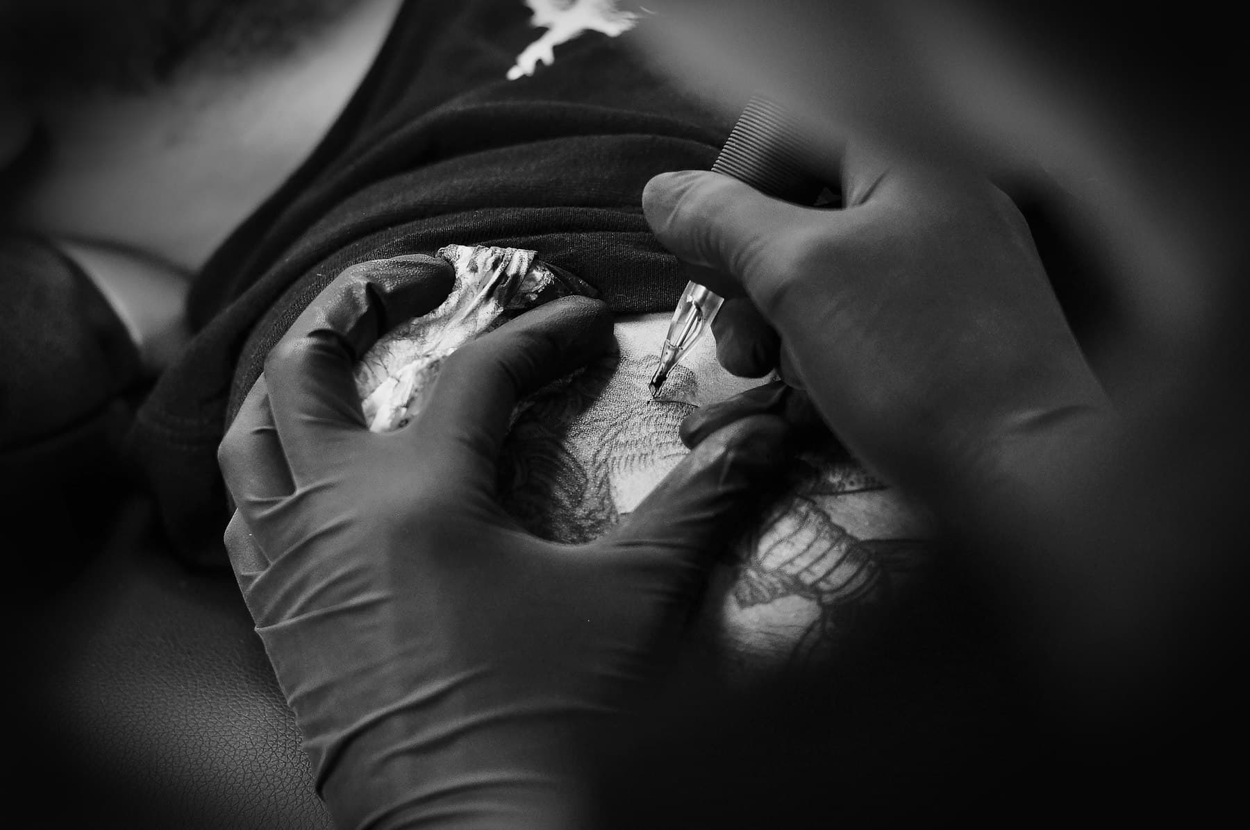Deux mains gantées au travail, en noir et blanc : l'aiguille suit le tracé.